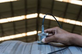 A hand holds an ultrasound probe on a curved metal surface that rises from the bottom of the image