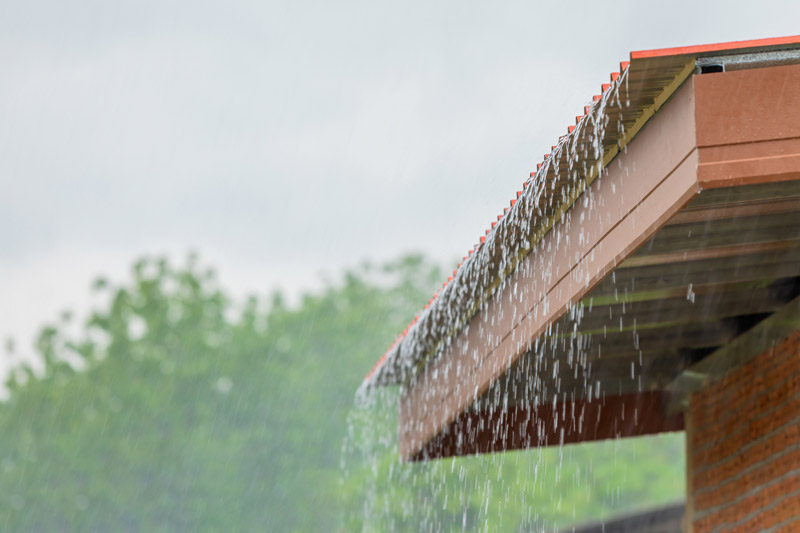 Rain water pours over the edge of a tile roof