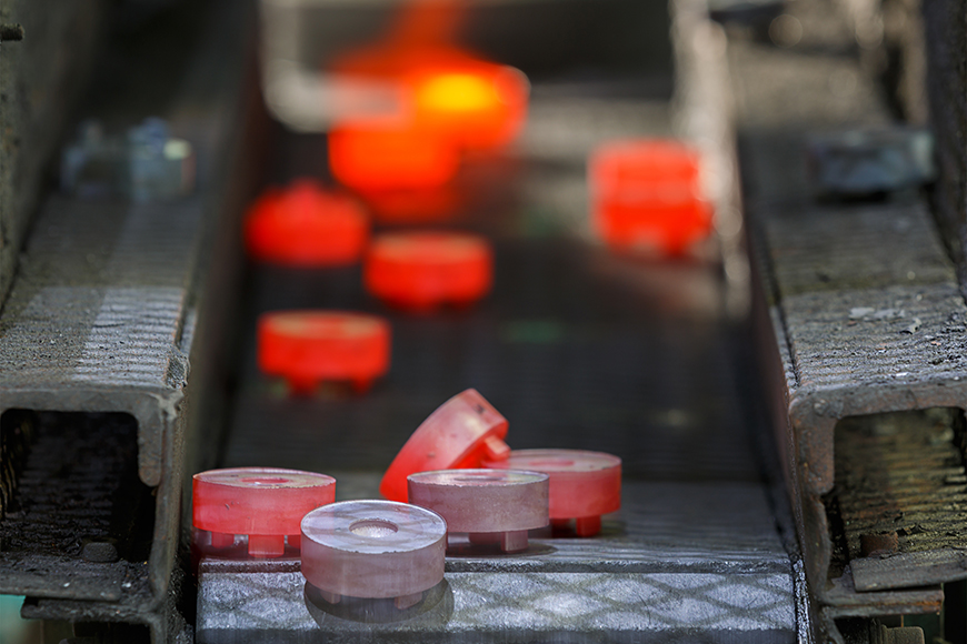 Steel gears glowing red with heat leave a furnace and cool to purple as they move down a conveyor